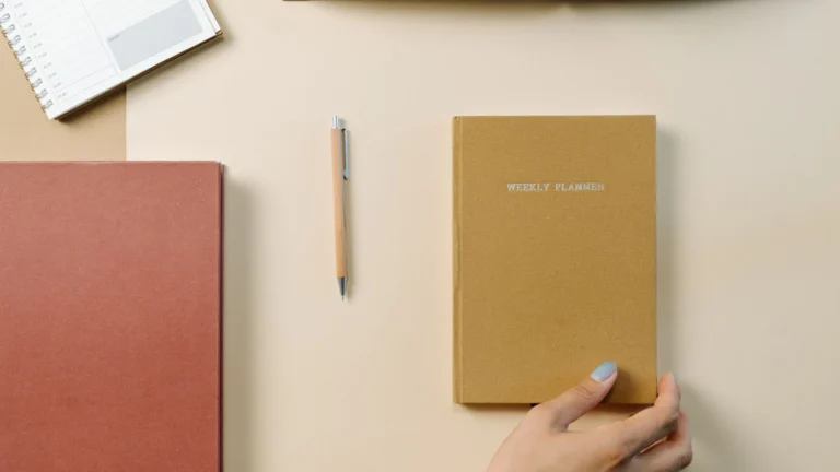 Weekly planner, notebook and pen arranged on a desk