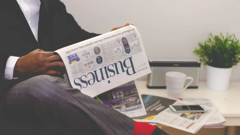 Reader examining a newspaper beside a smartphone and cup