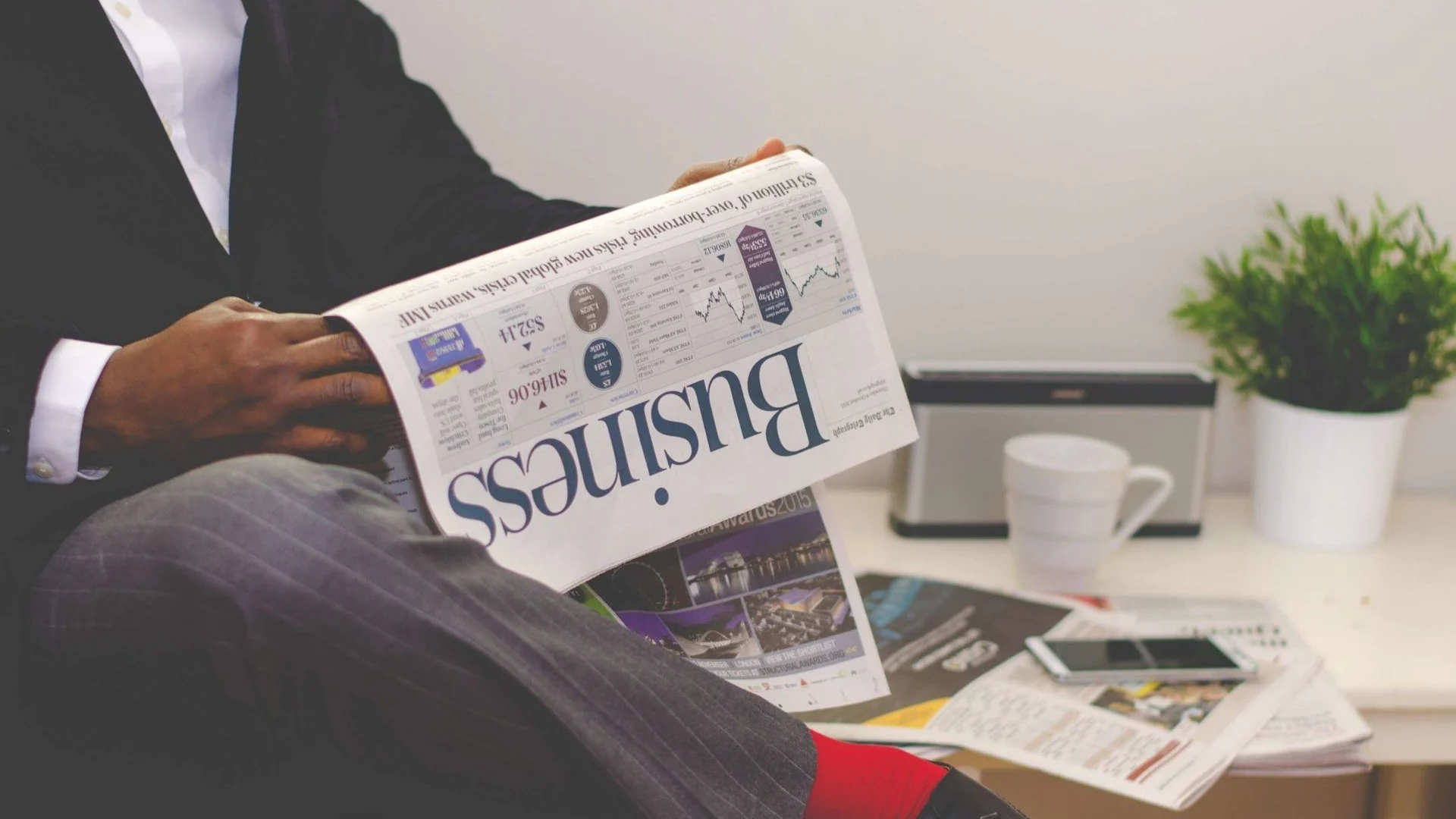 Reader examining a newspaper beside a smartphone and cup